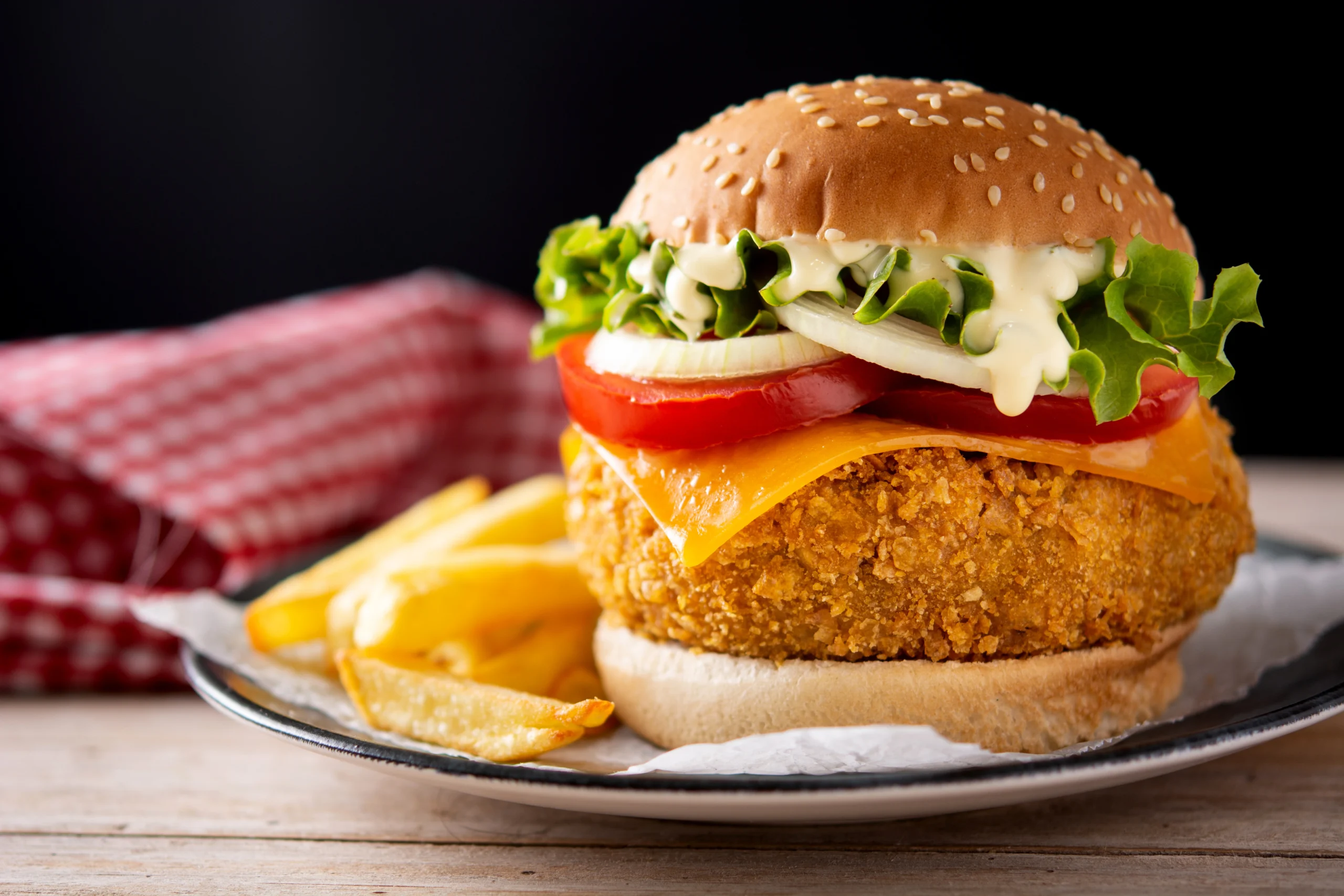 A close-up of a golden, perfectly crispy burger served with fresh lettuce, tomato, and melted cheese.